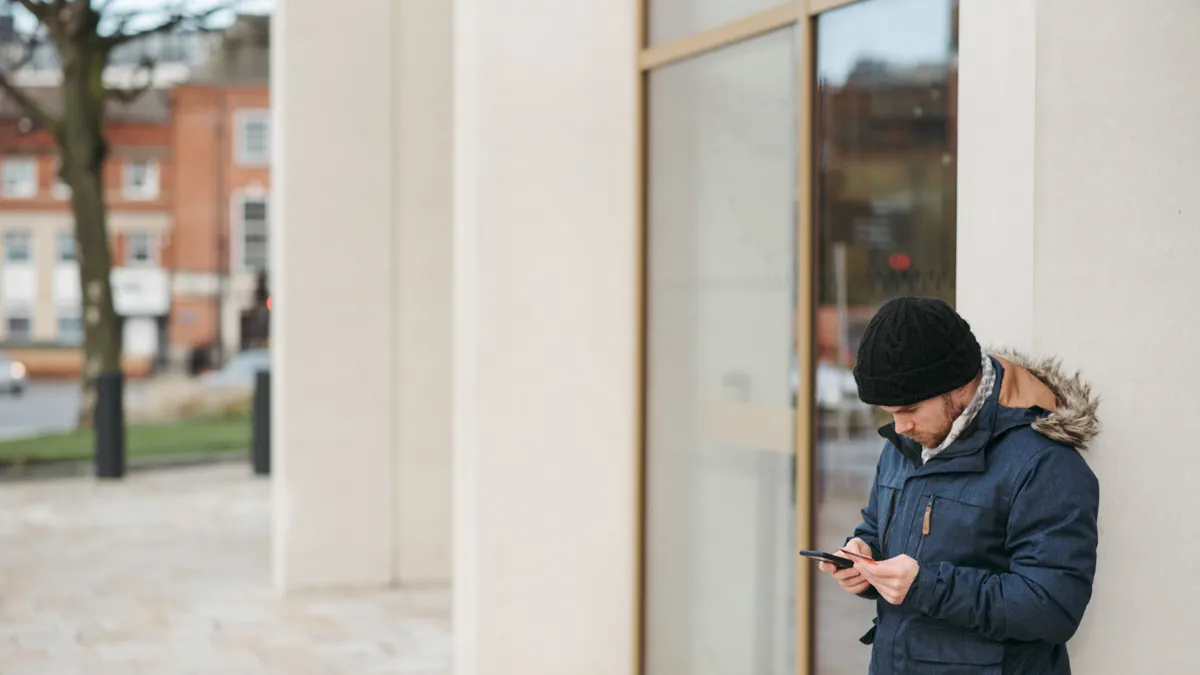 A man in a winter jacket reading a loan offer on his phone outside on a cold Regina day before deciding whether to sign